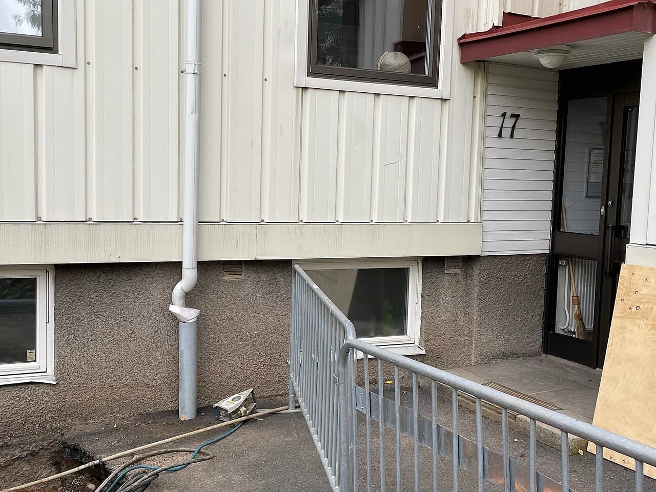 Nedløpsrør med løvfanger langs en trekledd boligvegg over synlig sokkel.