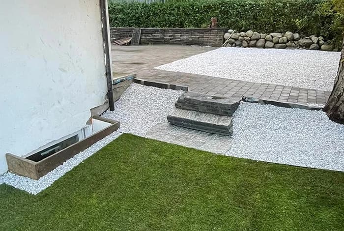 Uteområde ved hus med pukk, belegningsstein, trinn og grønn plen.